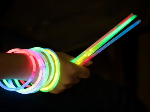 Hand holding glow sticks with glow bracelets on their wrist