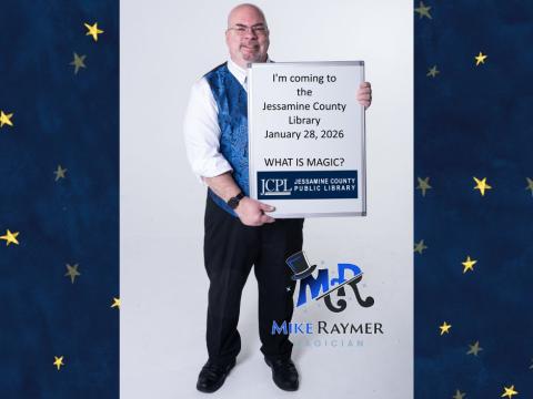 Mike Raymer magician holding sign saying he's coming to the library