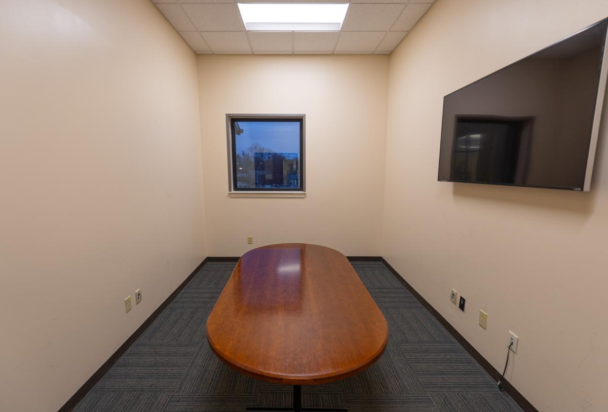 Small study room with a table in the middle and a 65" TV on the wall.